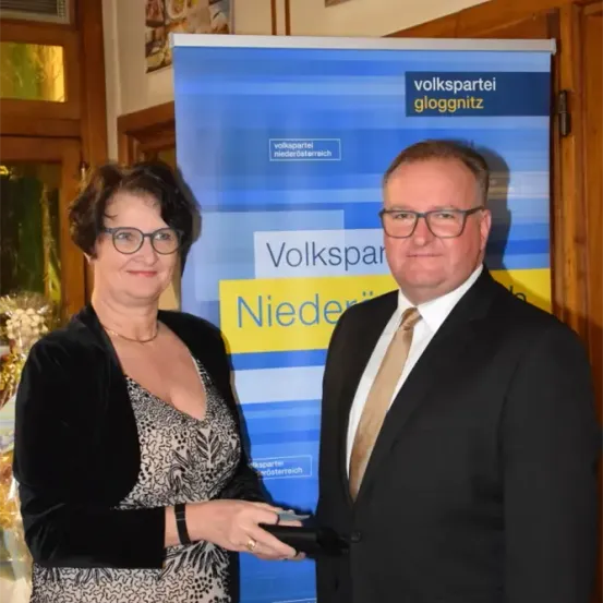 Eine Frau und ein Mann stehen lächelnd vor einem Volkspartei Niederosterreich-Banner. Die Frau hält ein Buch.