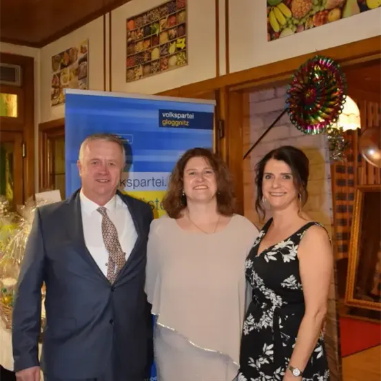 Drei Menschen stehen nebeneinander vor einem Banner. Ein Mann und zwei Frauen lächeln in die Kamera.