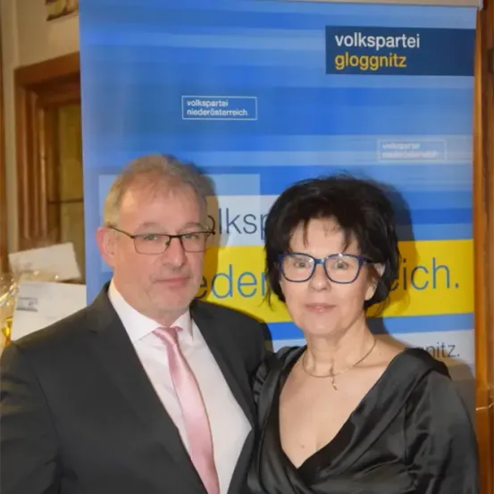 Ein Mann und eine Frau stehen nebeneinander, beide formell gekleidet. Sie lächeln für die Kamera. Hinter ihnen ist ein Banner mit dem Text 'volkspartei gloggnitz'.