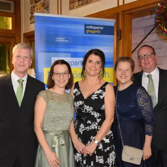 Fünf Personen posieren für ein Foto vor einem blauen Banner mit den Worten 'Volkspartei Gloggninz'. Drei Frauen und zwei Männer tragen formelle Kleidung. Die Frau in der Mitte trägt eine Uhr.