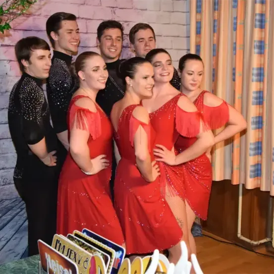 Eine Gruppe von Tänzern, sowohl Männer als auch Frauen, stehen zusammen und lächeln für ein Foto. Sie tragen rote Kleider.