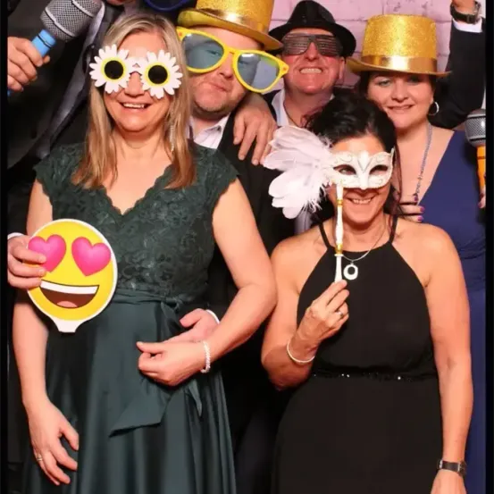 Gruppenfoto mit drei Frauen und drei Männern, alle in Kostümen und Masken gekleidet, halten ein Mikrofon und eine Smiley-Gesicht-Ausschnitt.