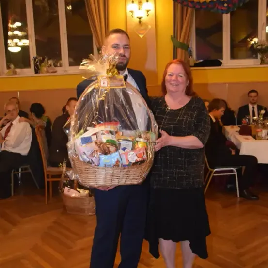 Ein Mann und eine Frau halten einen Korb voller verschiedener Snacks und stehen in einem Raum mit Holzböden und Tischen.