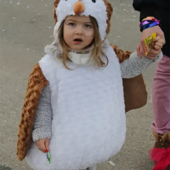Ein kleines Mädchen in einem flauschigen Pinguinkostüm hält eine Süßigkeit in der Hand und schaut zur Kamera.