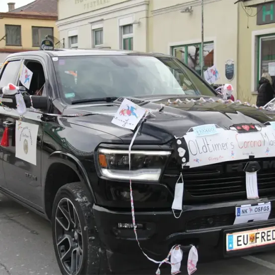 Ein schwarzer Pickup-Truck mit dekorativen Bändern und Schildern steht auf der Straße. Es steht Oldtimer's Corona Maskenwerfer und EU FRED 1 auf dem Stoßfänger.