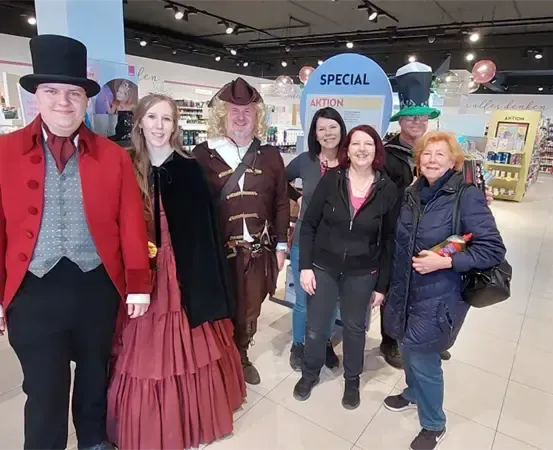 Eine Gruppe von Menschen in historischen Kostümen steht lächelnd für ein Foto in einem Geschäft.