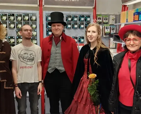 Fünf Personen in verschiedenen Kostümen, darunter ein Pirat und ein viktorianischer Gentleman, posieren für ein Foto in einem Geschäft.