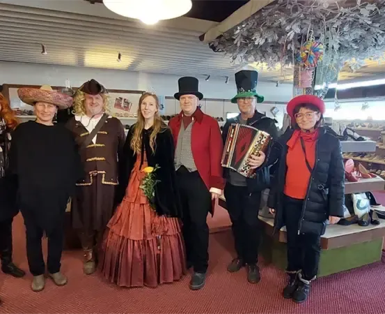 Eine Gruppe von Menschen in Kostümen, einschließlich Hüten, posiert für ein Foto in einem Raum mit rotem Teppich, Regalen und einer hängenden Dekoration.