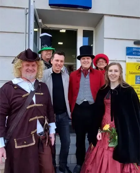 Sechs Menschen in verschiedenen Kostümen posieren für ein Foto vor einem UNIQA-Gebäude.
