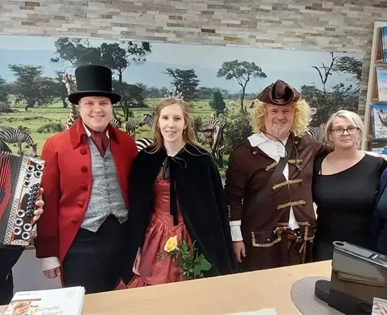 Gruppe von Menschen in Kostümen vor einer Kulisse, die eine Savanne mit Zebras und Bäumen darstellt.