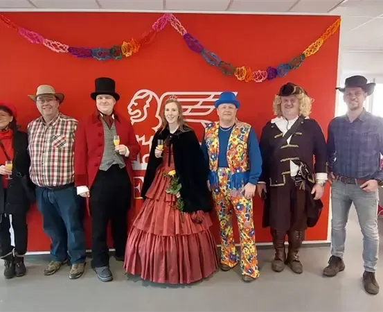 Gruppe von Menschen in Kostümen, die vor einer roten Wand für ein Foto posieren.