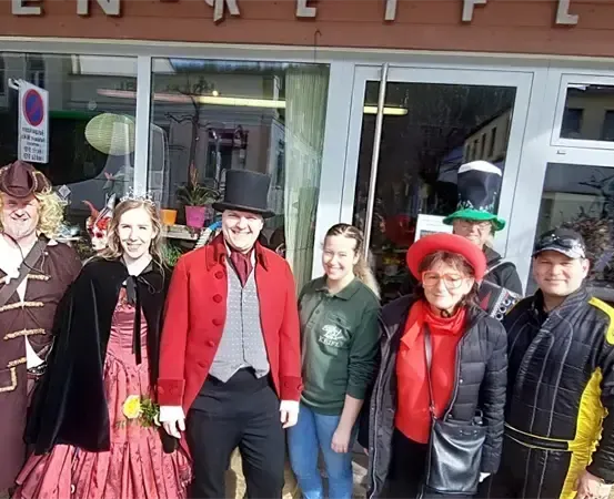 Eine Gruppe von Menschen in Kostümen steht vor einem Geschäft. Das Geschäft hat eine Glastür und Fenster.