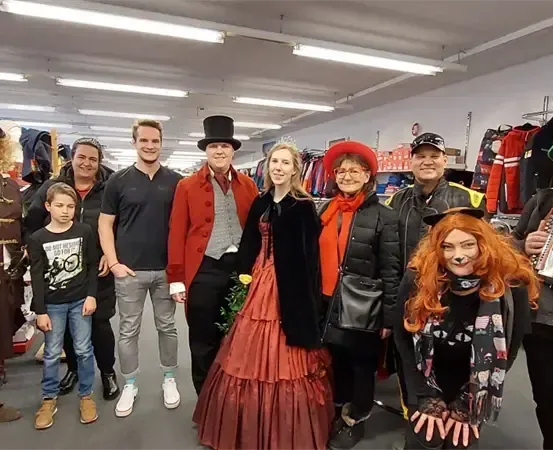 Eine Gruppe von Menschen in Kostümen posiert für ein Foto in einem Bekleidungsgeschäft mit beleuchteten Deckenleuchten.
