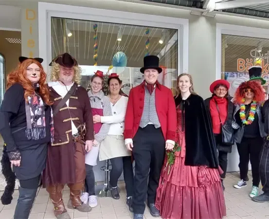 Eine Gruppe von Menschen in Kostümen steht vor einem Geschäft und posiert für ein Foto. Das Schild des Geschäfts lautet Bäckerei.