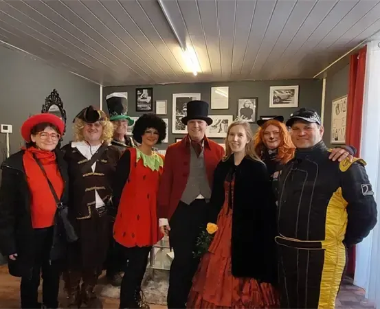 Eine Gruppe von Menschen in verschiedenen Kostümen steht in einem Raum mit grauer Wand und Decke.