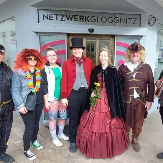 Eine Gruppe von Menschen in bunten Kostümen steht vor einem Gebäude mit dem Namen Netzwerkgloggnitz.