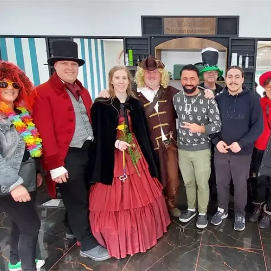 Eine Gruppe von Menschen in verschiedenen Kostümen, darunter ein Pirat, eine viktorianische Dame und ein Zylinderhut, steht vor einem Geschäft.