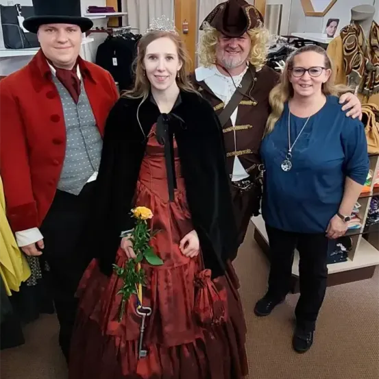 Vier Menschen in Kostümen, zwei Männer und zwei Frauen, posieren für ein Foto. Eine Frau hält eine Blume.
