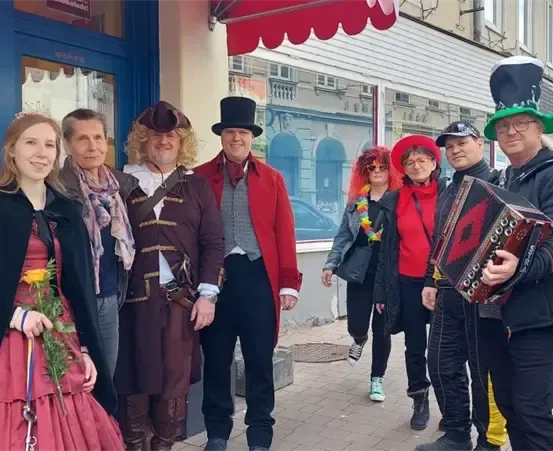 Eine Gruppe von Menschen in Kostümen und Hüten, die für ein Foto auf einem Bürgersteig vor einem Gebäude posieren.