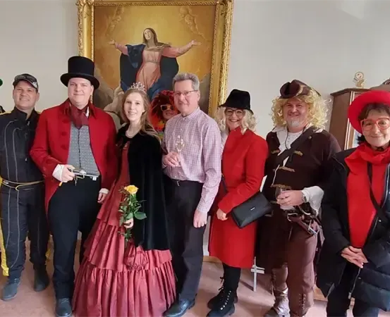 Eine Gruppe von Menschen in Kostümen posiert für ein Foto vor einer Wand mit einem großen Gemälde einer Frau.