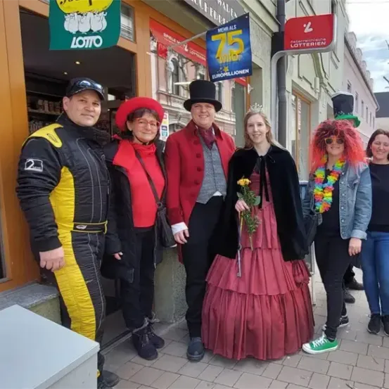 Eine Gruppe von Menschen in Kostümen posiert für ein Foto vor einem Geschäft mit einem Schild, das 'Lotterie' steht.