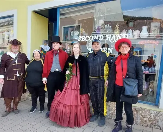 Eine Gruppe von Menschen in Vintage-Kleidung posiert für ein Foto vor einem Geschäft mit einem Schild, das Second Hand steht.
