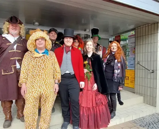 Eine Gruppe von Menschen in Kostümen steht vor einem Gebäude. Eine Person trägt ein Giraffenkostüm.