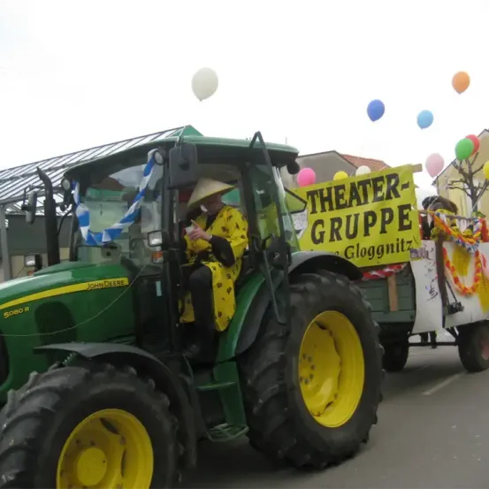 Ein Traktorkorso mit einer Person in einem gelben Outfit auf dem Fahrersitz, die einen Anhänger mit bunten Luftballons zieht.