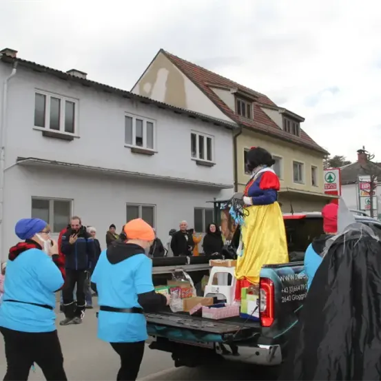 Eine als Schneewittchen verkleidete Person steht im Laderaum eines Pickup-Trucks, umgeben von Menschen in Kostümen. Sie nehmen wahrscheinlich an einem Umzug teil.