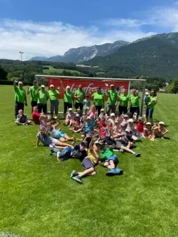 Eine Gruppe von Menschen in grünen Shirts posiert für ein Foto auf einem Rasenfeld mit Bergen im Hintergrund.