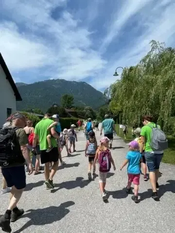 Eine Gruppe von Menschen, einschließlich Kinder mit Rucksäcken, gehen auf einer Straße mit Bergen im Hintergrund.