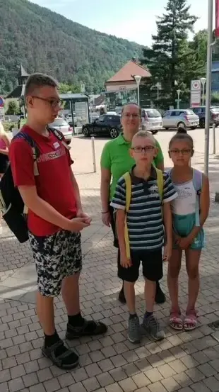 Vier Personen, zwei Erwachsene und zwei Kinder, stehen in einem Park mit einem Berg im Hintergrund. Sie tragen Freizeitkleidung und scheinen Touristen zu sein.
