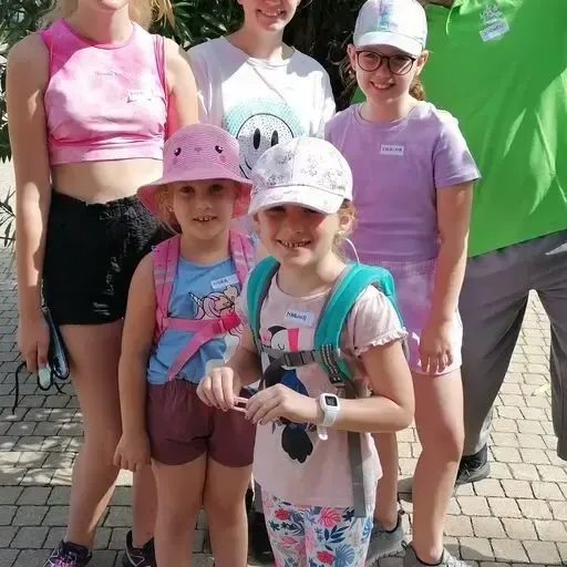 Eine Gruppe junger Mädchen und Jungen steht zusammen auf einem Ziegelboden. Sie lächeln und posieren für ein Foto. Sie tragen alle Freizeitkleidung.