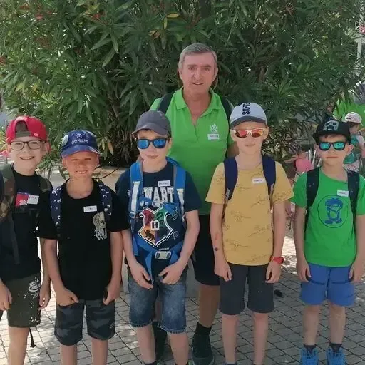 Eine Gruppe von Jungen und ein erwachsener Mann stehen draußen. Sie tragen alle Sonnenbrillen und Mützen. Sie lächeln und posieren für ein Foto.