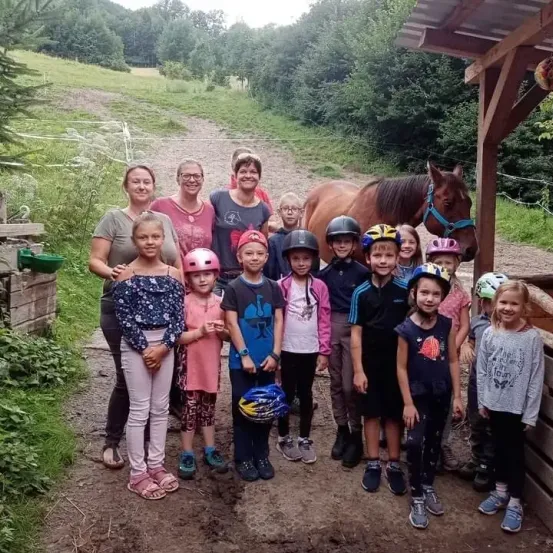 Eine Gruppe von Kindern und Erwachsenen steht auf einem Pfad im Wald mit einem Pferd. Sie tragen Helme, einige halten Helme.