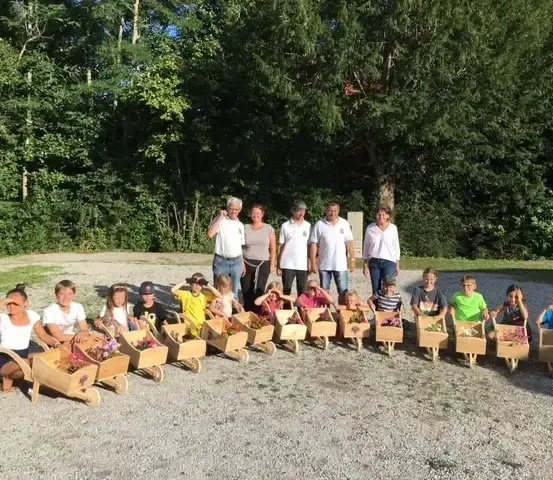 Eine Gruppe von Menschen, darunter Kinder, posiert für ein Foto mit ihren blumengefüllten Schubkarren in einem Park.