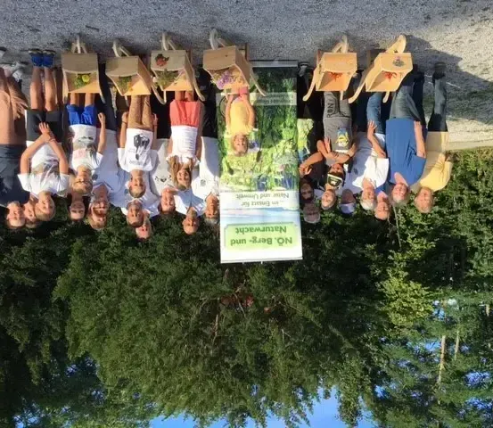 Eine Gruppe von Menschen posiert für ein Foto mit Holzkisten auf dem Kopf, vor Bäumen stehend.