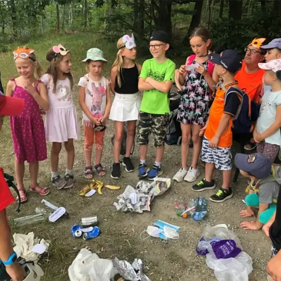 Eine Gruppe von Kindern und Erwachsenen versammelt sich um einen Haufen Müll auf einem Erdweg, in Freizeitkleidung und teilweise mit Mützen.
