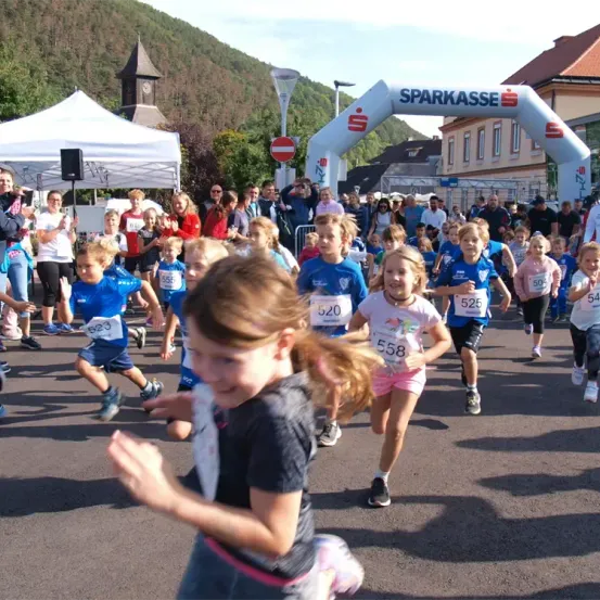 Kinder laufen in einem Marathon. Sie tragen Nummern auf ihren Trikots. Zuschauer feuern sie an.