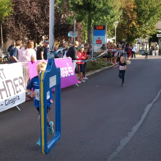 Ein Marathonläufer beendet den Lauf mit anfeuernden Zuschauern. Eine digitale Uhr zeigt die Zeit an. Ein weiterer Läufer führt das Rennen an.
