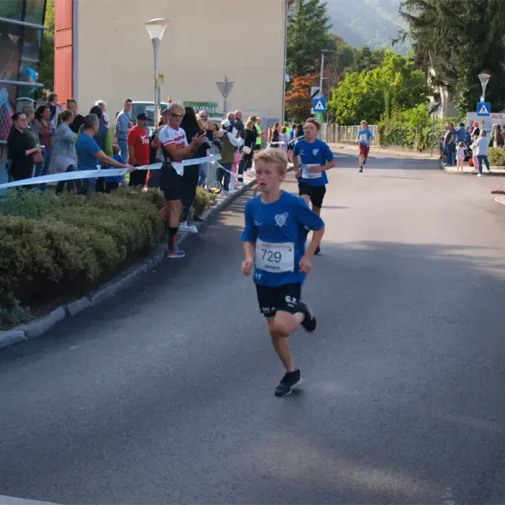 Ein junger Junge mit der Nummer 729 läuft bei einem Marathon, mit Zuschauern am Straßenrand.