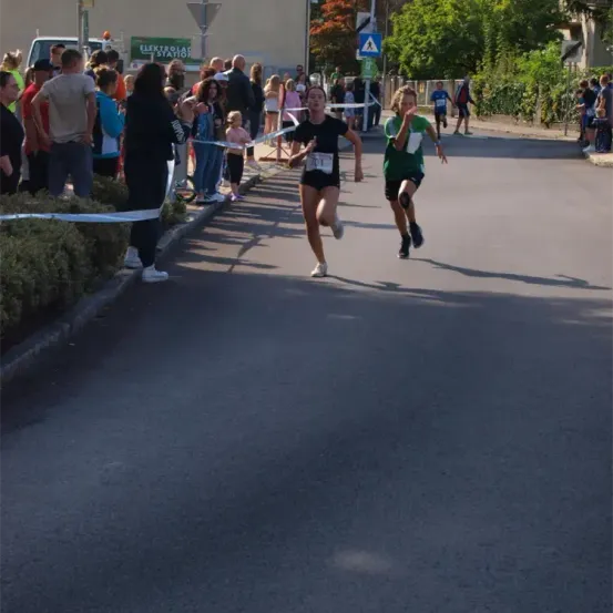 Läufer nehmen an einem Marathon teil, begleitet von einer jubelnden Menge. Eine Frau führt das Rennen vor einem jungen Mädchen an.