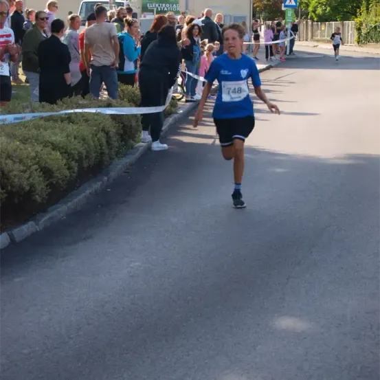 Ein Läufer mit der Nummer 748 läuft in einem Rennen, während Zuschauer am Straßenrand zusehen.