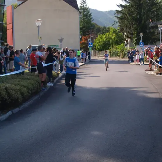 Ein Marathonläufer sprintet die Straße hinunter, mit Zuschauern auf beiden Seiten, einige halten Bänder, um den Weg zu markieren. Der Läufer trägt die Nummer 718 auf seinem Trikot.