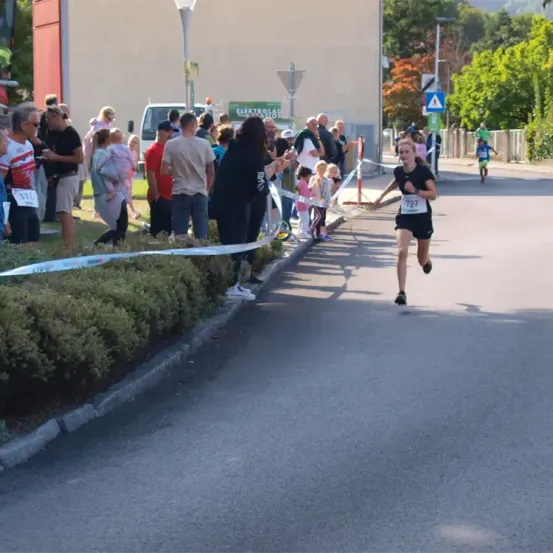 Ein Läufer mit der Nummer 727 läuft auf der Straße, während die Menschen von der Seite anfeuern. Einige Leute stehen hinter einer Seilbarriere.