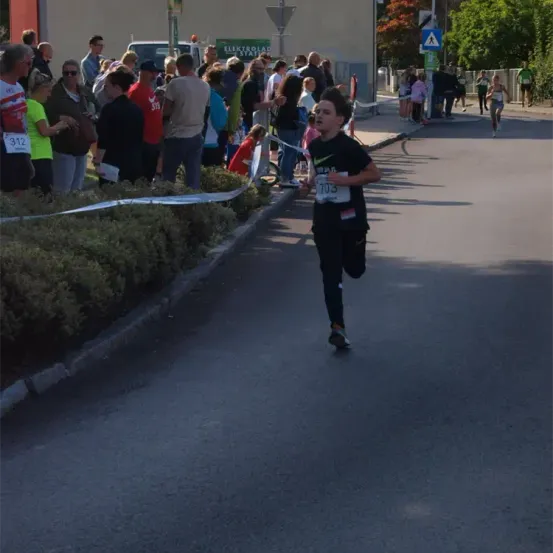 Ein Läufer mit der Nummer 703 nimmt an einem Marathon teil. Zuschauer beobachten von der Straßenseite.