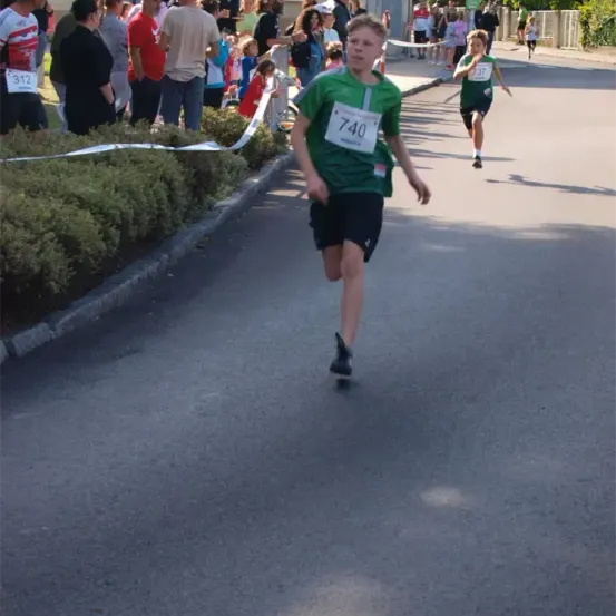 Ein Läufer mit der Nummer 740 läuft die Straße hinunter, während Zuschauer von den Seitenlinien zusehen.