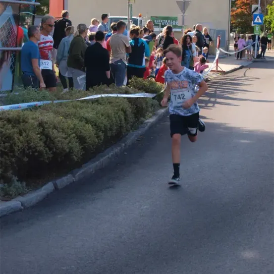 Ein junger Junge mit der Nummer 742 auf seinem Shirt läuft in einem Rennen. Zuschauer säumen die Straße, einige mit Nummern auf ihren Shirts.