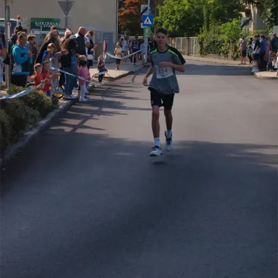 Ein Läufer mit der Nummer 714 auf seinem Trikot läuft bei einem Rennen, das von einer Menge jubelnder Menschen an der Seite angefeuert wird.