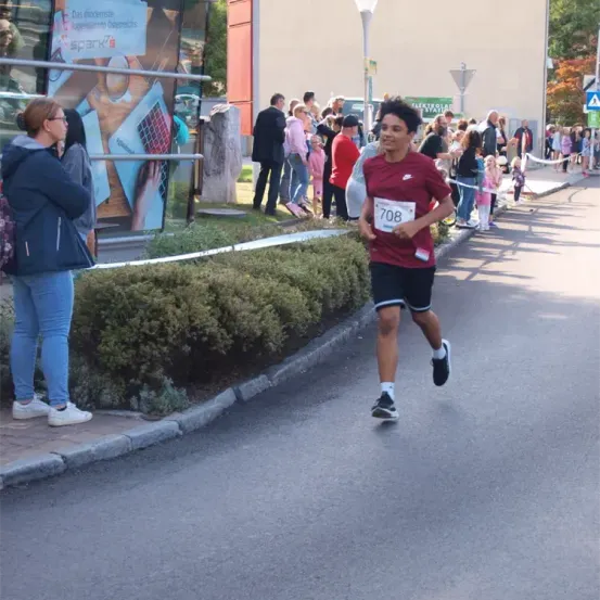 Ein Läufer mit der Nummer 708 läuft auf der Straße, während Menschen herumstehen und zuschauen.